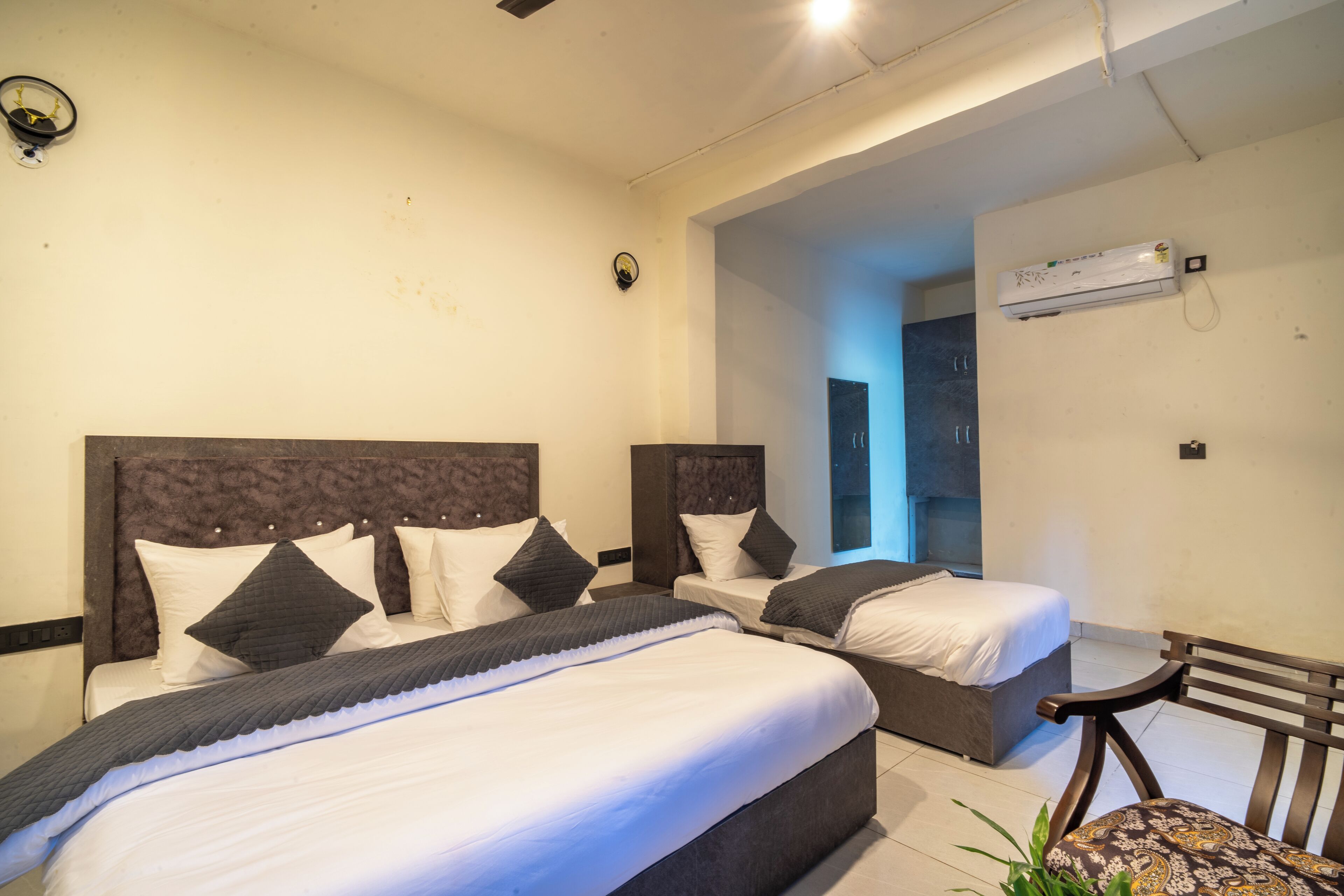 A hotel room with two beds, a bench, and an air conditioning unit.
