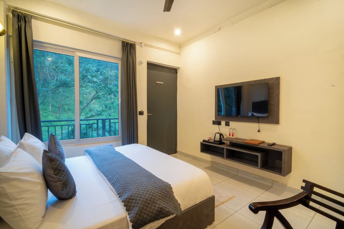 A bedroom with a large bed, a TV mounted on the wall, a window with curtains, and a bench.