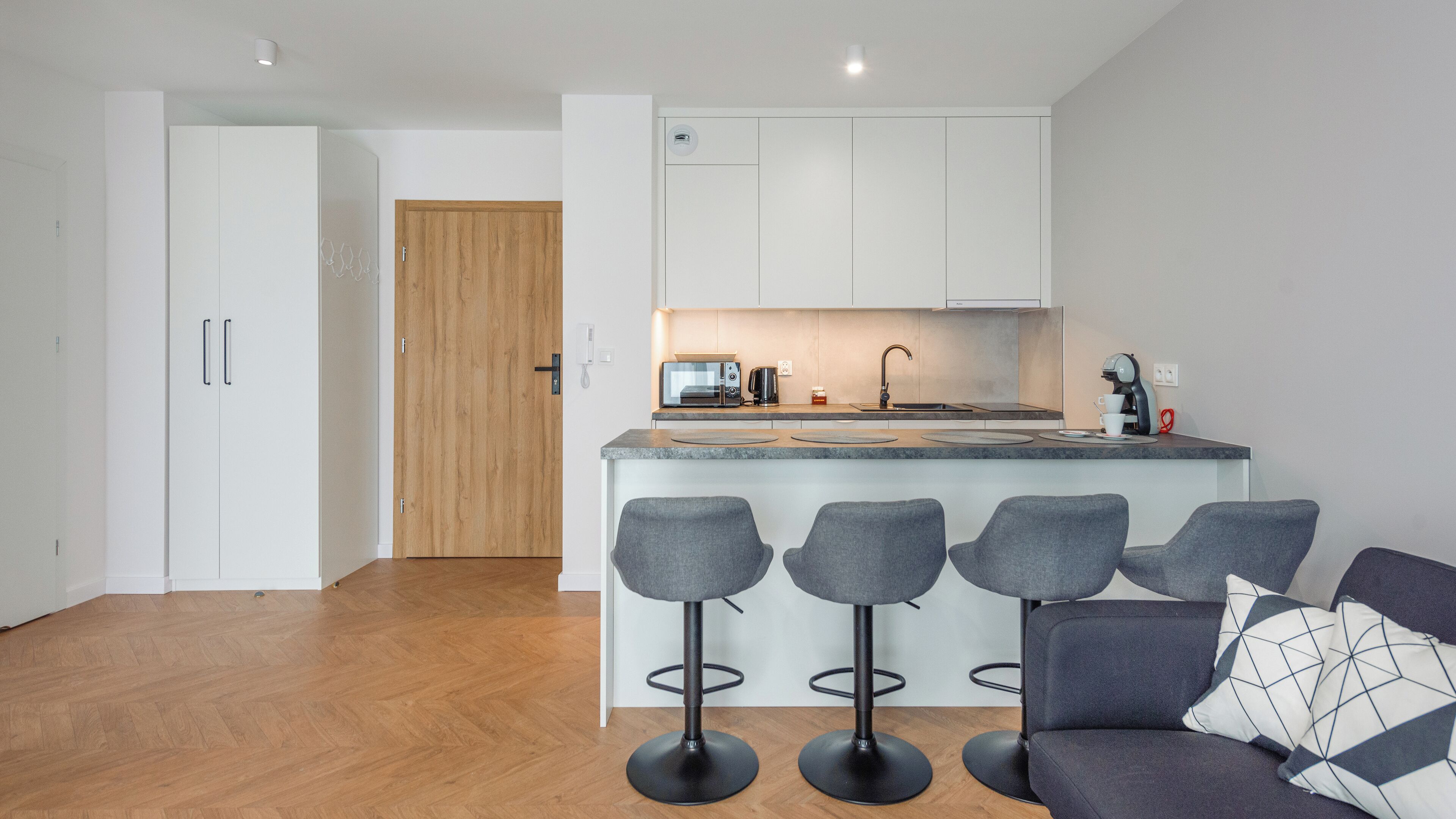 A modern kitchen with a central island, bar stools, and a sofa with a geometric pillow.