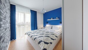 A modern bedroom with a brick wall, a large window with blue curtains, a bed with a geometric-patterned duvet, and a blue accent wall. - Apartamenty Sun & Snow Kuracyjna Jastrzębia Góra (Wladyslawowo)