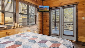 Een gezellig kamer in een blokhut met een groot bed, houten wanden en een aan de muur bevestigde televisie.