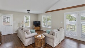 A spacious living room with a high ceiling, a flat-screen TV, two beige sofas, a wooden coffee table, and large windows with blinds. - Serenity on the Lake (Prosperity)