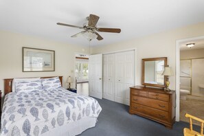 A bedroom with a bed, dresser, ceiling fan, and a door leading to a bathroom. - Serenity on the Lake (Prosperity)