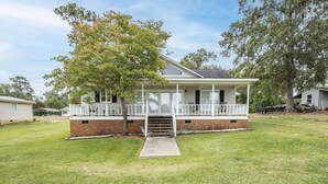 A single-story house with a front porch, a brick foundation, and a grassy yard. - Serenity on the Lake (Prosperity)