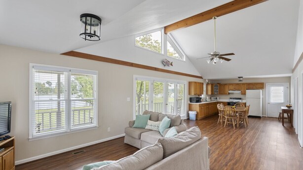 A spacious living area with a high ceiling, wooden beams, a sofa set, a dining table, and a kitchen in the background. - Serenity on the Lake (Prosperity)