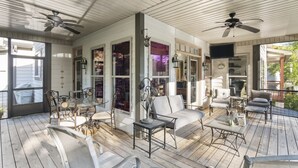 A covered porch with a dining table, chairs, a sofa, and ceiling fans.