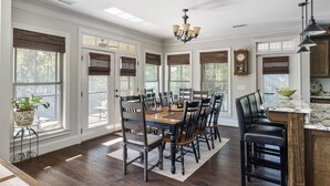 A spacious dining area with a large wooden table, multiple chairs, and a chandelier.