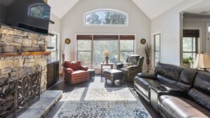 A spacious living room with a stone fireplace, leather sofa, and a large window providing natural light.