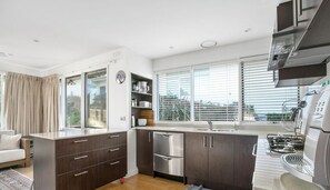 A modern kitchen with dark cabinetry, a stainless steel refrigerator, and a built-in oven. - Portsea Reserve House (Portsea)