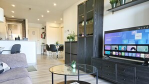 A modern living room with a flat-screen TV displaying a home screen, a glass coffee table with a magazine, a grey sofa, and a kitchen area in the background. - Two bedroom apartment in Riviera del sol (Mijas Costa)