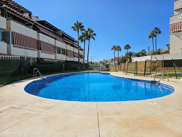 A swimming pool with a curved edge, surrounded by a stone wall and palm trees. - Two bedroom apartment in Riviera del sol (Mijas Costa)