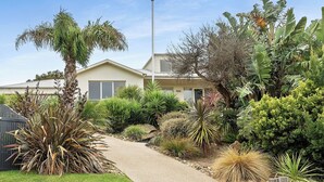 Il s'agit d'une propriété résidentielle dotée d'une allée pavée, de diverses plantes tropicales et d'une maison à l'extérieur de couleur claire.
