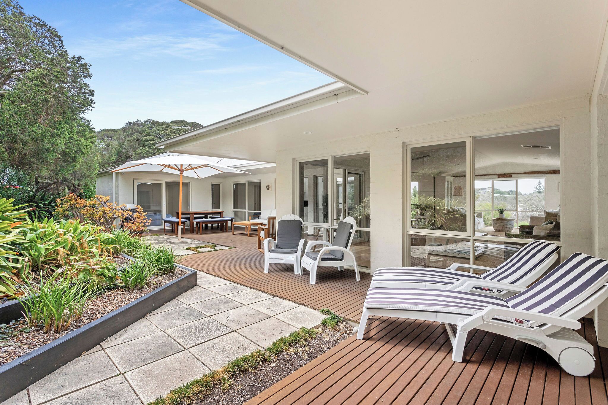A modern outdoor deck with lounge chairs, a dining area, and a covered patio.