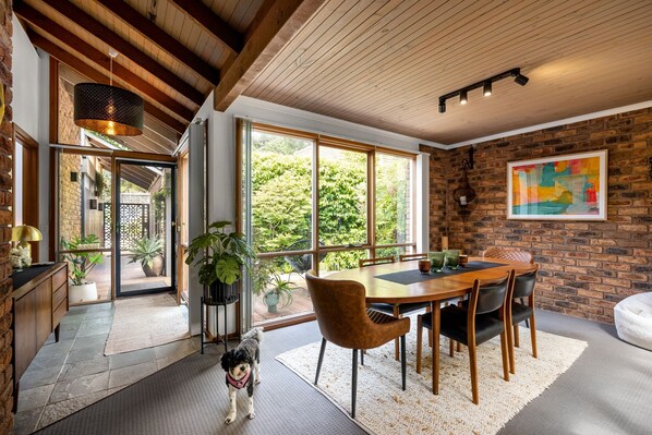 Enjoy meals in a warm dining area with a wooden table and chairs, surrounded by lush greenery views.