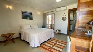 A bedroom with a bed, a wooden bench, a small stool, a rug, and a painting on the wall. - Camaleao Ecopousada Ltda (Linhares)