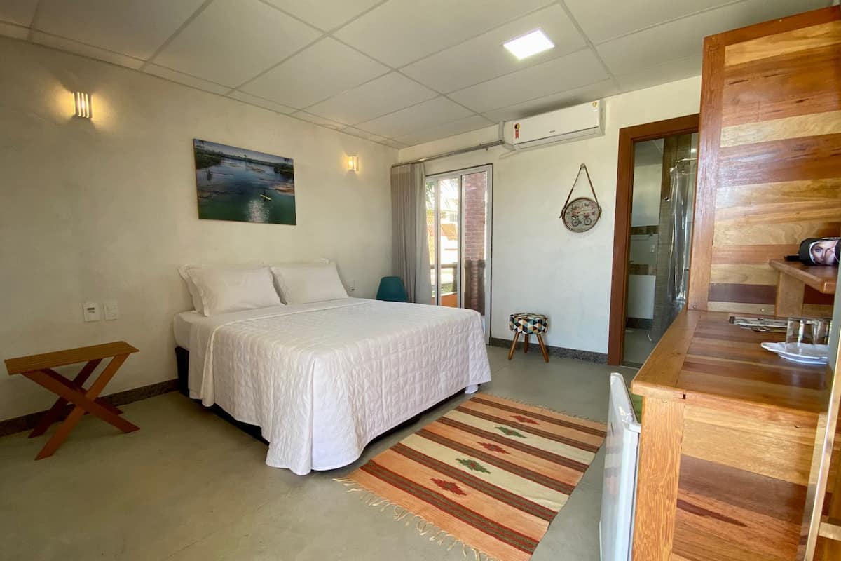 Un dormitorio con cama, un banco de madera, un taburete pequeño, una alfombra y un cuadro en la pared.