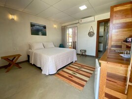 Um quarto com uma cama, um banco de madeira, um banquinho, um tapete e um quadro na parede.
