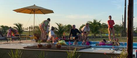 Zona de piscina con gente disfrutando del agua, rodeada de macetas y mobiliario de exterior.