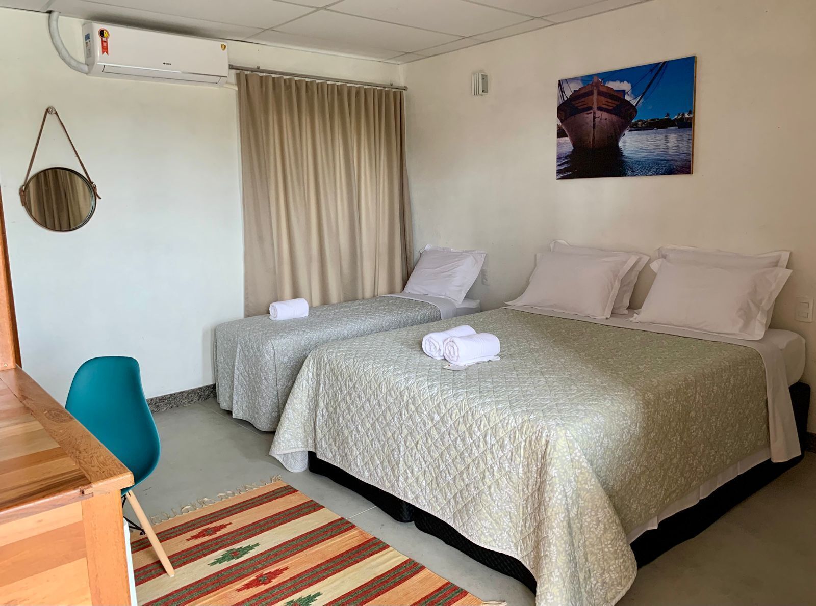Habitación de hotel con dos camas, un escritorio, una silla, una cesta colgante y un cuadro en la pared.