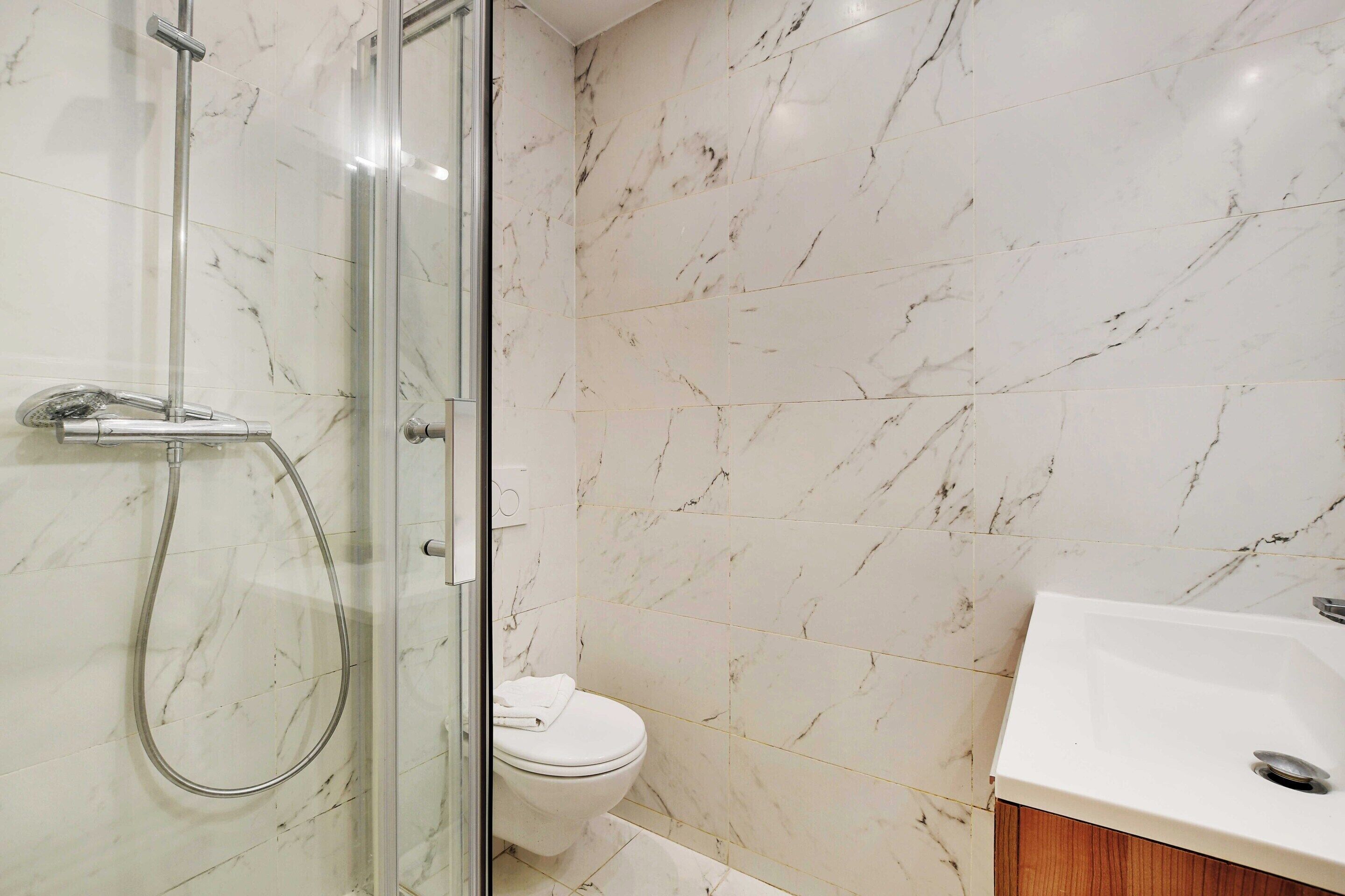 Une salle de bain avec une douche à parois de verre, des toilettes blanches et un lavabo avec un meuble en bois.