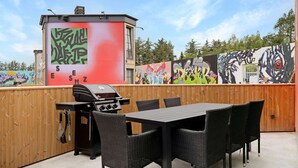 An outdoor patio with a grill, wicker furniture, and a mural on the wall. - Holiday Home in Blokhus Near Theme Park (Blokhus)
