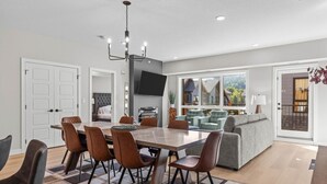 Un salon moderne comprenant un coin repas, une grande fenêtre et une vue sur une maison.