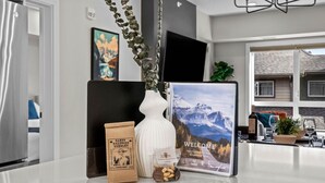 Un comptoir de cuisine avec un sac de café, un vase blanc orné de verdure et un panneau d’accueil offrant une vue sur la montagne.