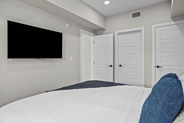 Un dormitorio con una cama, un televisor de pantalla plana en la pared y dos puertas blancas.