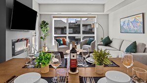 Un salon moderne avec une table à manger dressée pour le repas, une cheminée et une grande fenêtre donnant sur des maisons.