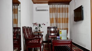 A traditional living room with wooden furniture, a small table, and a TV mounted on the wall. - Royal Park Hotel (Kumasi)
