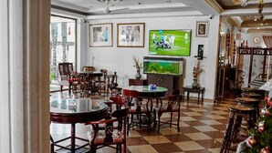 A dining area with checkered flooring, wooden chairs, a television mounted on the wall, and a Christmas tree. - Royal Park Hotel (Kumasi)