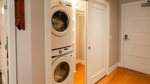 Une buanderie avec deux machines à laver superposées, une porte blanche et un plancher en bois.