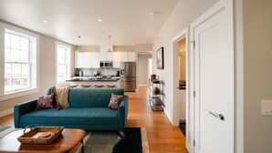 Un soggiorno moderno con un divano verde acqua, un tavolino in legno e una cucina sullo sfondo.