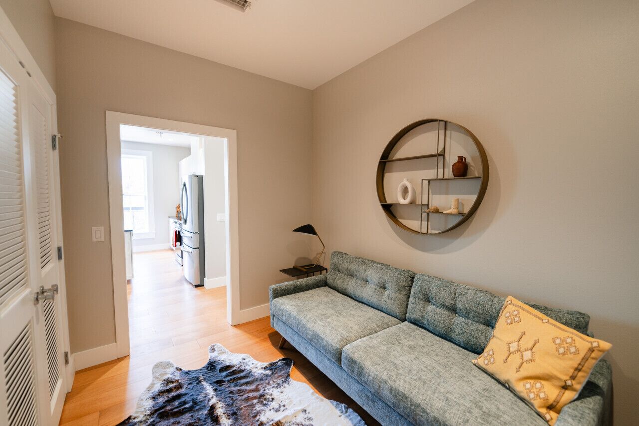 Ein Wohnzimmer mit einem grauen Sofa, einem runden Spiegel und einem Teppich.