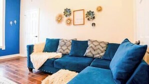 Een woonkamer met een blauwe bank, decoratieve wandkunst en een houten vloer.