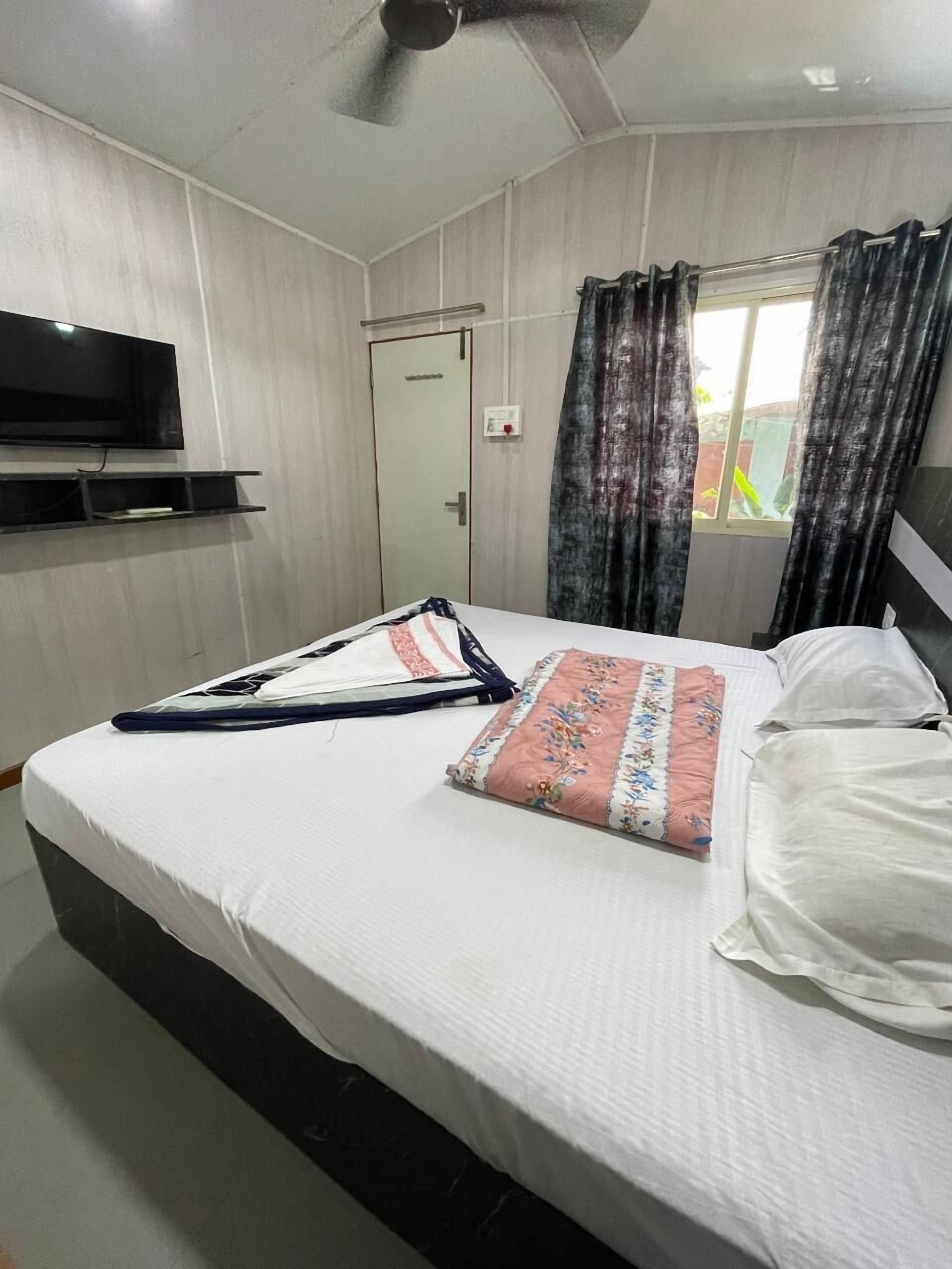 A hotel room with a bed, a flat-screen TV mounted on the wall, a window with curtains, and a door.