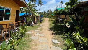 A pathway leading to a wooden building with a balcony, surrounded by tropical vegetation and palm trees. - Sydney X cafe and Huts (Arambol)
