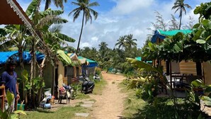 A rural village with thatched-roof huts, a dirt path, and palm trees. - Sydney X cafe and Huts (Arambol)