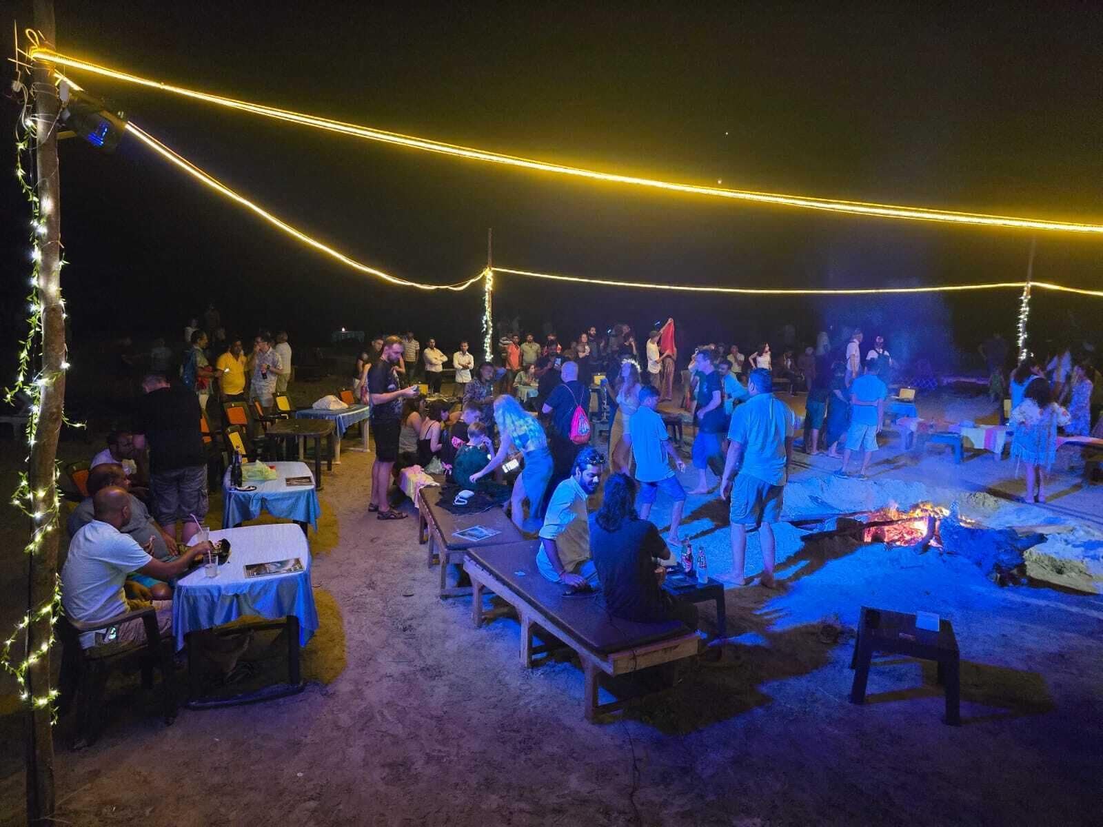 Un espace extérieur aménagé avec des tables et des bancs, illuminé par des guirlandes lumineuses.