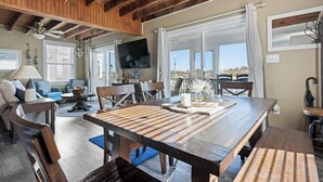 Amplia sala de estar con una mesa de comedor de madera, asientos cómodos, un televisor y ventanas grandes que ofrecen vistas al exterior.