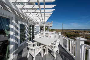 Une terrasse extérieure couverte, avec une table et des chaises blanches, donnant sur une plage.