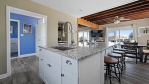 Una cocina moderna con armarios blancos, encimeras de granito y una isla central con taburetes de bar.