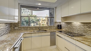 A modern kitchen with a large window, granite countertops, stainless steel appliances, and a view of buildings outside.