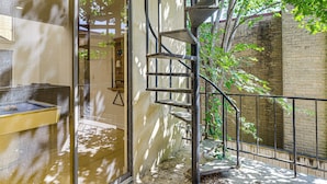 A spiral staircase leading to an outdoor area with a pool, surrounded by a brick wall and greenery.