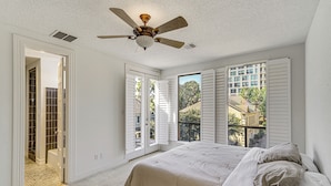 A bedroom with a bed, a ceiling fan, and a view of the outside.