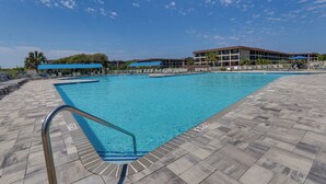 Une piscine avec une terrasse carrelée, un poste de surveillance pour les sauveteurs et un bâtiment avec un toit bleu en arrière-plan.