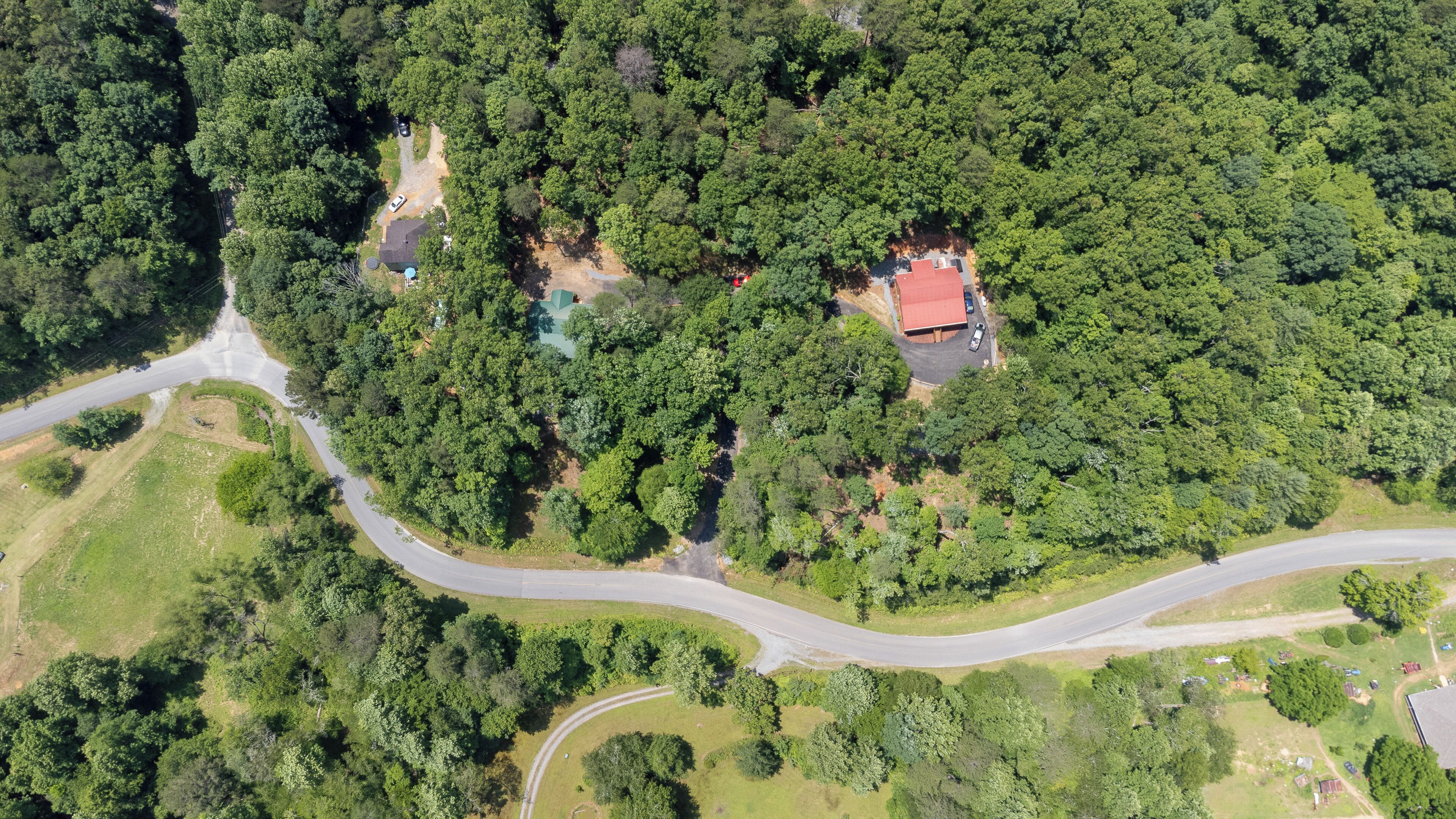 Ett flygbildsfoto av en fastighet med en slingrande väg, en tät skog och en byggnad med ett rött tak.