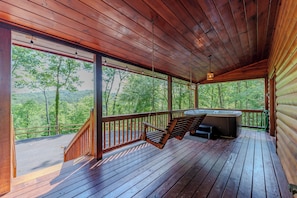 A wooden deck with a hot tub, a swing, and a view of the forest.