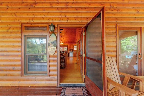 A wooden cabin with a welcoming sign, a porch with a chair, and a view of the interior. - Cottage w/ Hot Tub: 3 Mi to Downtown Blue Ridge! (Blue Ridge)
