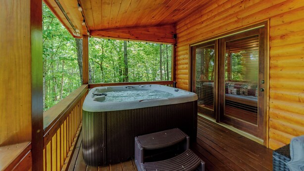 Eine Holzhütte mit Whirlpool, einer Terrasse und einer Glastür, die in einen bewaldeten Bereich führt.